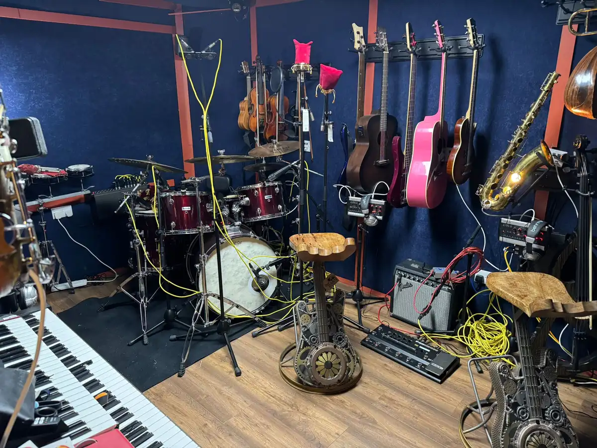 The instrument wall at 4chordsStudios: violins, acoustic guitars and a saxophone above the drum kit